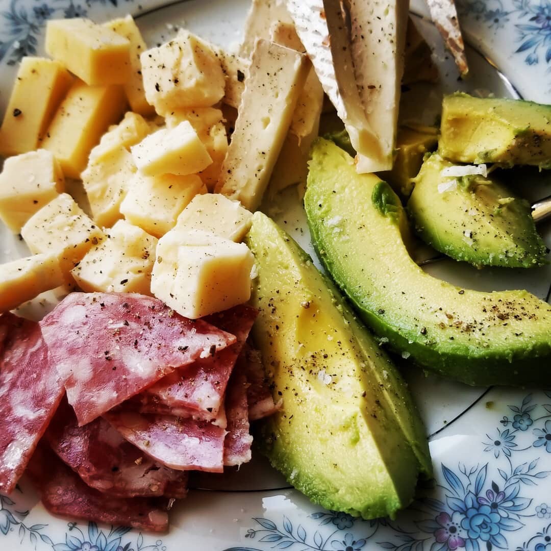 a vibrant colored plate of food full of cheese blocks, avocado and cured meat 