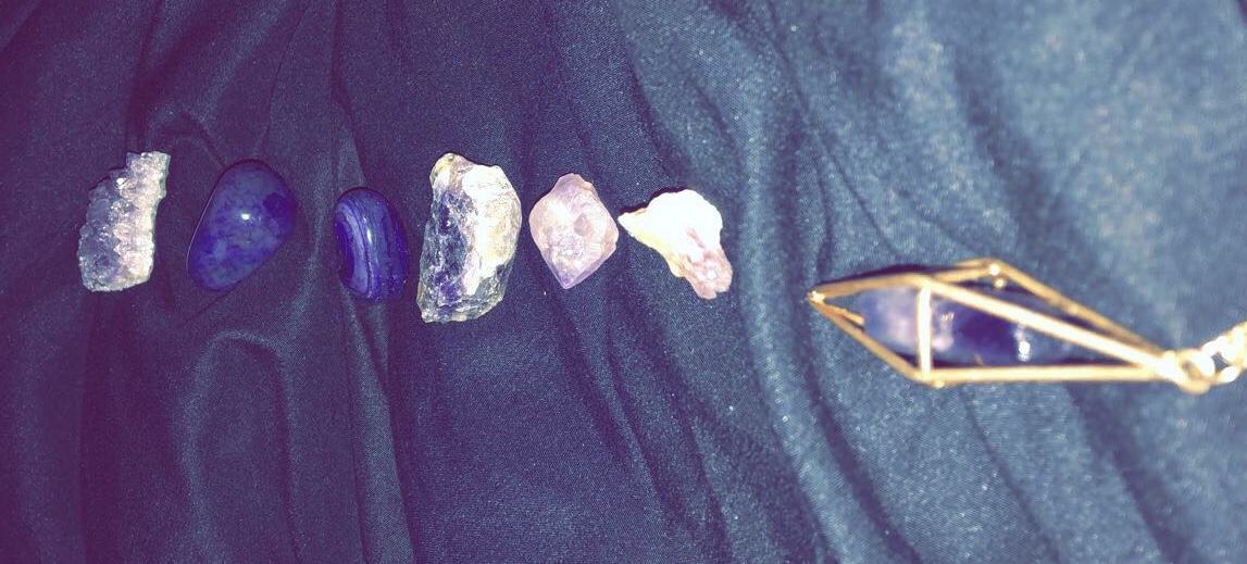 a line of purple amethyst tumbles and raw stones meeting an enclosed amethyst necklace 