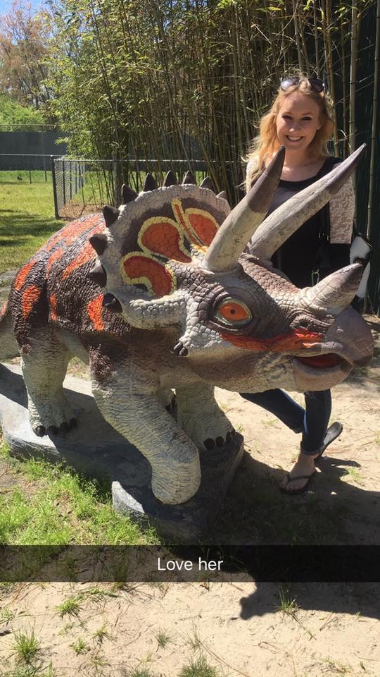 Large Triceratops standing in front of blonde girl with black top on.