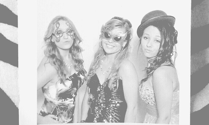 Black and white clipping of a photobooth printout with three girls in fancy gowns wearing funny glasses. 
