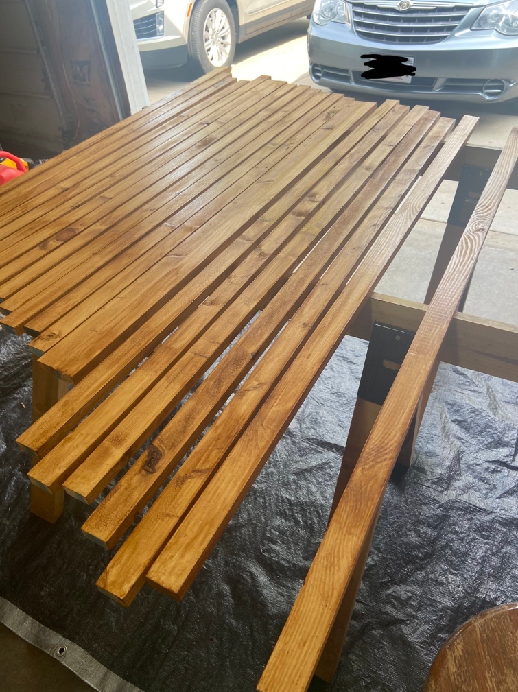 A few dozen boards laid across their stands with a single coat of stain on them, they are now a darker warm toned color the notches and variation of the pine beneath still showing through adding character.